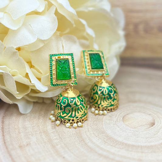 Green and gold earrings on a wooden surface with white flowers in the background